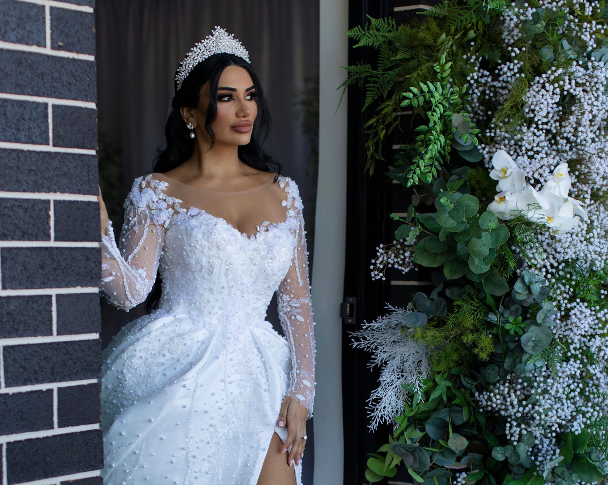 A lovely woman in a wedding gown standing in front of a wall, wearing sparkling Hayal  bridal tiara