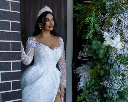 A lovely woman in a wedding gown standing in front of a wall, wearing sparkling Hayal  bridal tiara