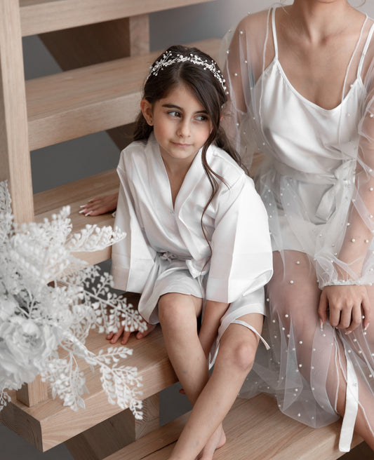 A beautiful girl wearing a white flower girl robe sitting beside a woman